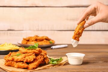 Woman dipping tasty nugget into sauce on wooden table