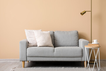 grey sofa with cushions, lamp and table near beige wall