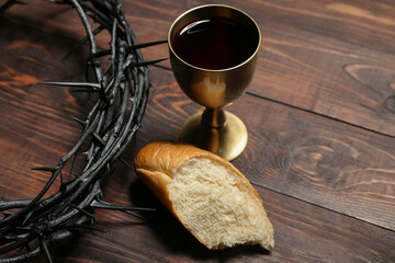 Wall Mural - Crown of thorns with cup of wine and bread on wooden background, closeup