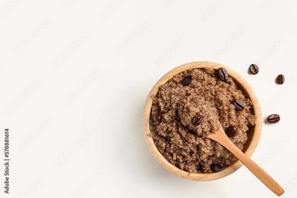 Bowl of body scrub and coffee beans on light background