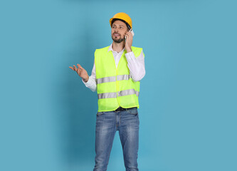 Poster - Male industrial engineer in uniform talking on phone against light blue background