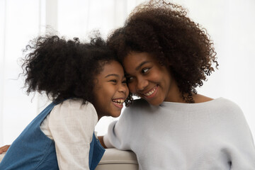 happy family embracing together on sofa at home. smiling african american young mother spending time