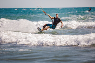 Professional kiter does the difficult trick. A male kiter rides against a beautiful background of waves and performs all sorts of maneuvers.