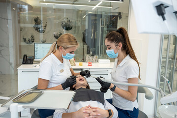 female dentist and an assistant treat the teeth of a young female patient.