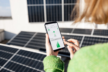 Woman monitors energy production from the solar power plant with mobile phone. Close-up view on phone screen with running program. Concept of remote control of solar energy production