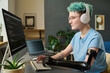 © AnnaStills - Young developer in wireless headphones typing security codes on computer sitting at her workplace at home