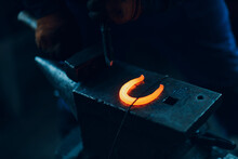 Blacksmith Forges And Making Metal Horseshoe With Hammer And Anvil At Forge.