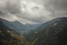 A Bridge Spanning A Valley In The Swiss Alps Under A Stormy Sky