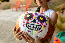 Girl Holds Big Pumpkin With A Dia De Los Muertos Skull Painted On It