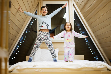 Children in soft warm pajamas playing at wooden cabin home. Concept of childhood, leisure activity, happiness. Brother and sister having fun and playing together.