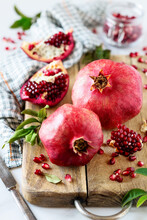 Red Ripe Pommegranates On A Wooden Cutting Board With Split Open Fruit Pieces And Juicy Seeds