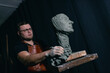© primipil - Man sculptor creates sculpt bust clay human woman sculpture. Statue craft creation workshop.