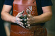 © primipil - Man sculptor dressed leather apron with clay in hands. Statue craft creation workshop.