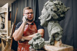 © primipil - Man sculptor creates sculpt bust clay human woman sculpture and calling client cell mobile phone