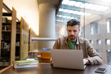 Pensive latin student studying, using laptop computer, learning language, exam preparation sitting in library. Successful middle aged copywriter working freelance project online at workplace  