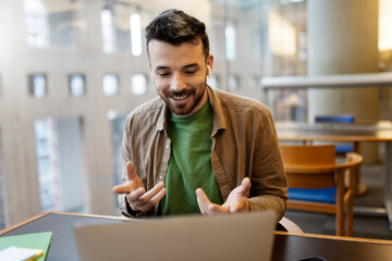 Handsome smiling latin man using laptop computer explaining something having video call. Successful bearded influencer recording video. Happy student studying, online lesson, education concept 