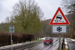Car passing on a wet road in winter with a slippery road and ice warning sign