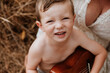 © Austockphoto - Young boy sitting on mother's lap in long grass, smiling up at camera