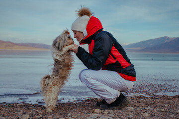 Wall Mural - Young woman tourist with dog posing on frozen lake background at winter