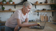 © RZ Images - Portrait of elderly woman in pink t-shirt standing at the kitchen and using laptop