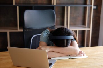 Tired Asian student girl lying on table in front of laptop, sleeping, taking break during online learning. Female freelancer napping at home office, feeling lazy to work remotely. Selective focus