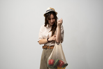 Wall Mural - Zero waste concept. A young girl holds on her hand a textile mesh eco bag with a groceries. The girl smiles, wearing a beige t-shirt and hat. Refusal of plastic bags.