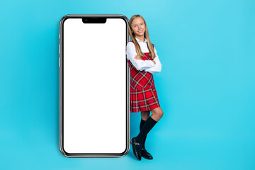 Poster - Full length portrait of cheerful charming schoolchild crossed hands showing empty space screen isolated on blue color background