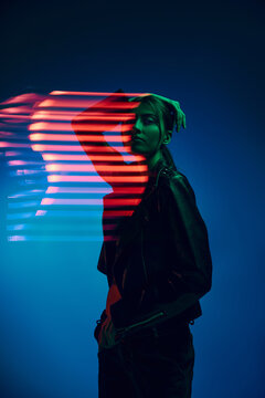 half-length portrait of young stylish woman posing over dark blue background with neon mixed light l