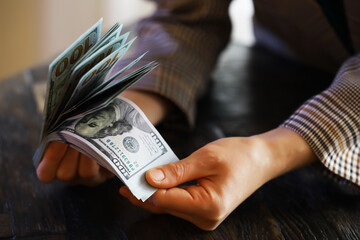 Female hands counting American one hundred dollar bills against the background of smaller bills of money lying on the table