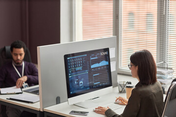High angle view of two office workers at desk with partition wall, focus on data on computer screen