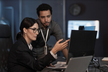 portrait of senior project manager pointing at computer screen while reviewing code in office