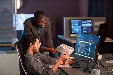 Two male IT engineers discussing documentation at workplace in office and reviewing code
