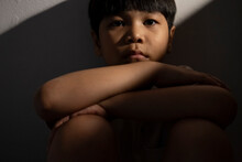 Portrait Of A Asian Kid Sitting Alone And Looking At The Camera. Homesick Or Sadness Or Broken Family Concept. Lowlight Shot Available Light
