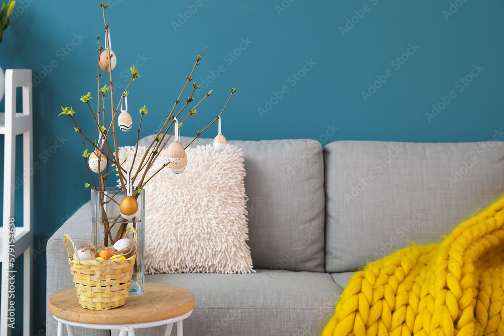 Vase with tree branches, Easter eggs and basket on table in living room