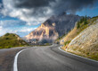 Mountain road at sunny day in summer. Dolomites, Italy. Beautiful roadway, green tress, high rocks in clouds, blue sky. Landscape with empty highway through the mountain pass in spring. Travel