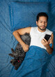 © Narayan - latin man using cell phone in bed with his dog, cell phone concept