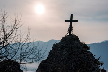 wooden cross with chain on rock formation with cloudy sky and bright sun in the background during su