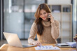 © David - Attractive successful young business Asian woman in striped blouse working in modern office, making phone call to potential client, having nice conversation, sitting at desk in front of open laptop