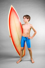 Wall Mural - Smiling boy in blue swim trunks holding his surfboard under one arm