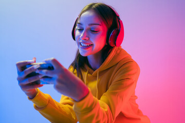 A young Caucasian beautiful woman in a yellow hoodie playing a video game using a joystick and headphones with fun, focus, surprise, and a winning victory face with blue and red neon light.