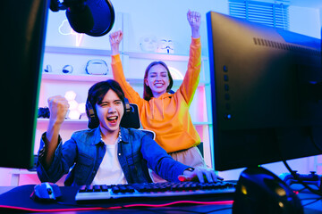 Asian male gamer and Caucasian woman coach celebrating victory together in front of the gaming table. Gamer winning an esports game with mentor. The player rejoices in victory in the competition.