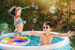 Children blow soap bubbles while swimming in a home pool.