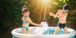 Happy children splashing water in inflatable home pool in summer. Outdoor active recreation.