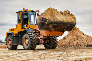 Wall Mural - Powerful wheel loader or bulldozer working on a quarry or construction site. Loader with a full bucket of sand. Powerful modern equipment for earthworks.