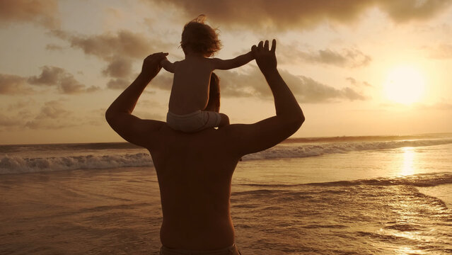 family idyll - father playing with his little son on beach during sunset, carrying him on his should