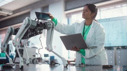 Fototapete - Young Indian Female Engineer Testing Industrial Programmable Robot Animal in a Factory Development Workshop. Professional Researcher in a Lab Coat Developing AI Canine Prototype, Using Laptop