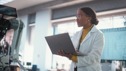 Poster - Portrait of Young Black Female Specialist in a Lab Coat Smiling and Using Laptop Computer. Professional and Successful Woman Working as an Engineer, Developing High Technology Projects