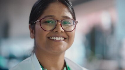 Poster - Portrait Close Up of Young Indian Female Specialist Wearing Lab Coat and Glasses Smiling. Professional and Successful Woman Working as an Engineer, Science Student in University Laboratory Posing