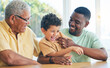 © Charlize D/peopleimages.com - Black family grandfather, child and father playing, having fun and enjoy time together in Angola home. Bonding, love and happy African generation of kid son, grandpa and dad tickling laughing boy