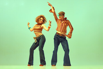 two excited people, man and woman in retro style clothes dancing disco dance over green background. 